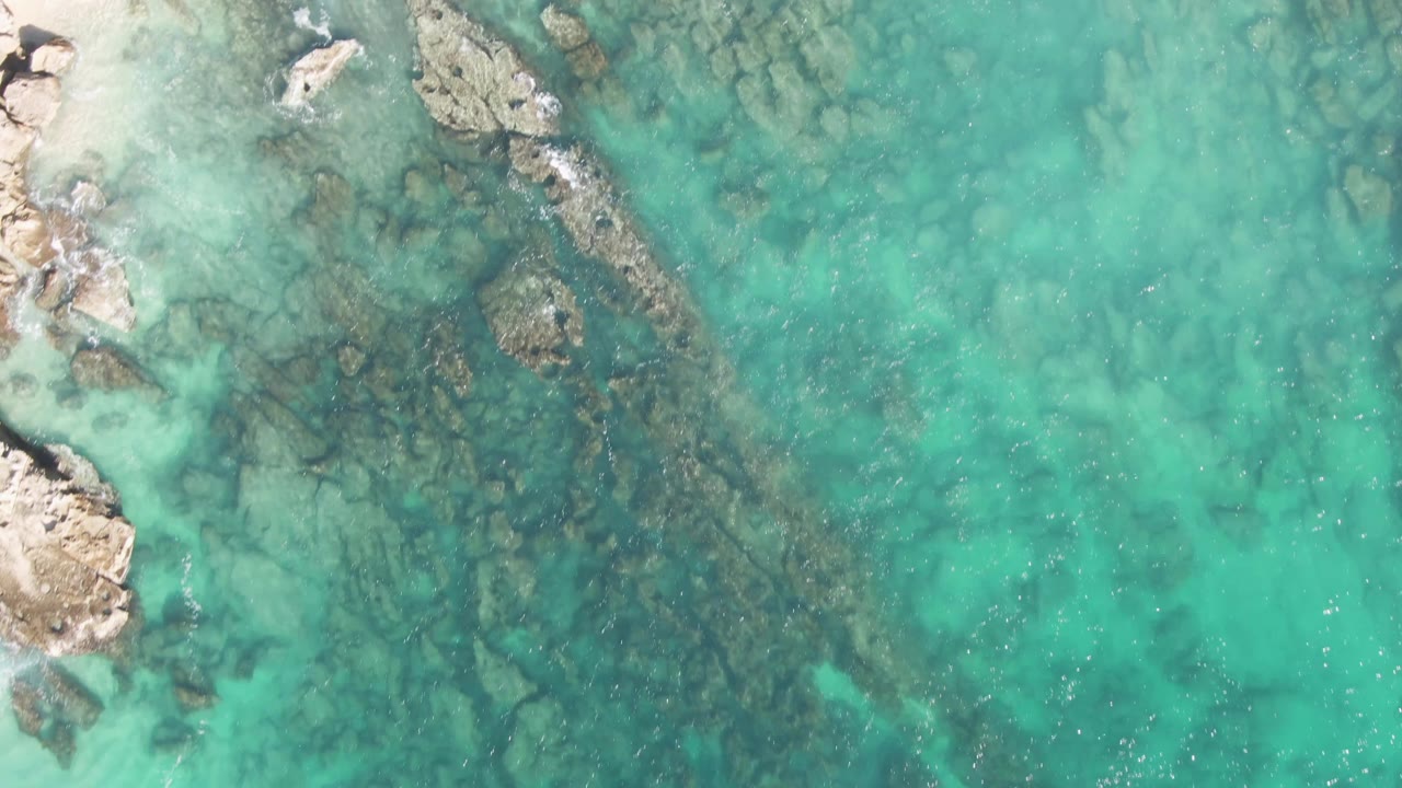 Clear turquoise water with submerged rocky ridges and pale rocks along the left side.