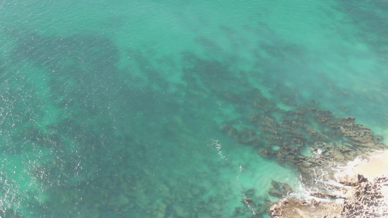 Turquoise water over submerged rocks beside a rocky shore
