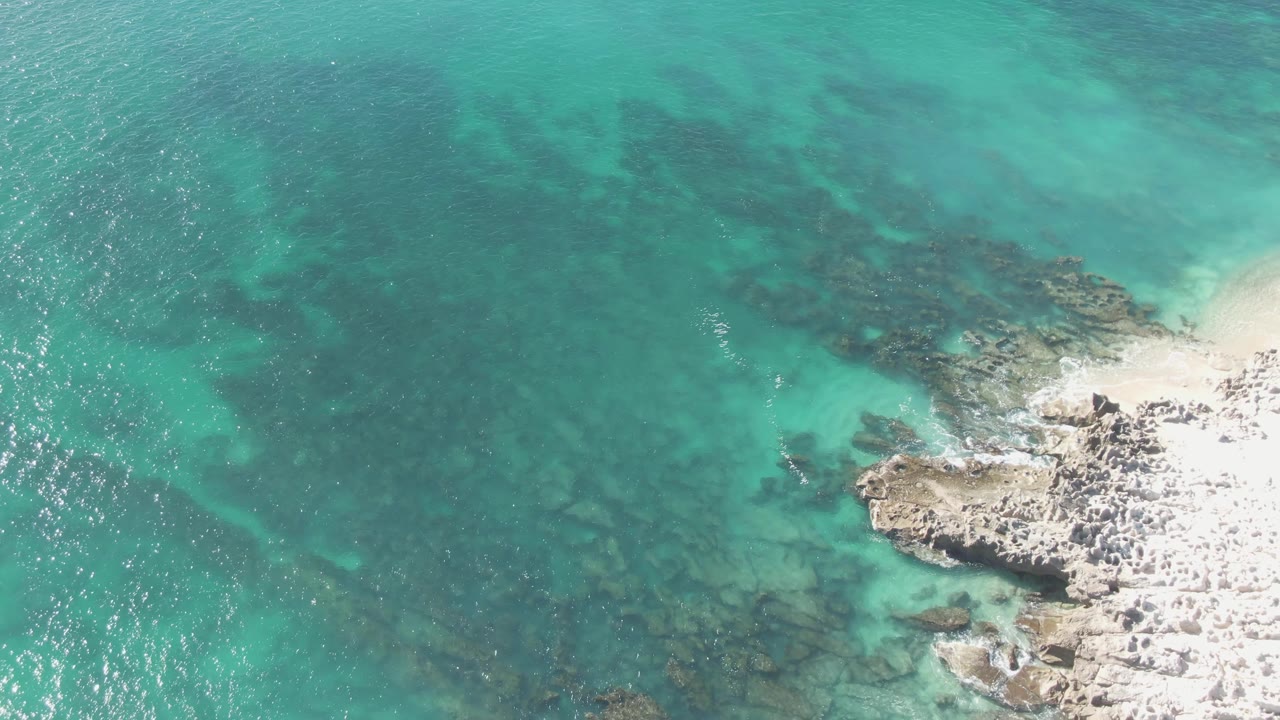 At Buzzards Beach in Baja California Sur, turquoise water fills the left side while pale rock and sand form the shore on the right, with no visible people.
