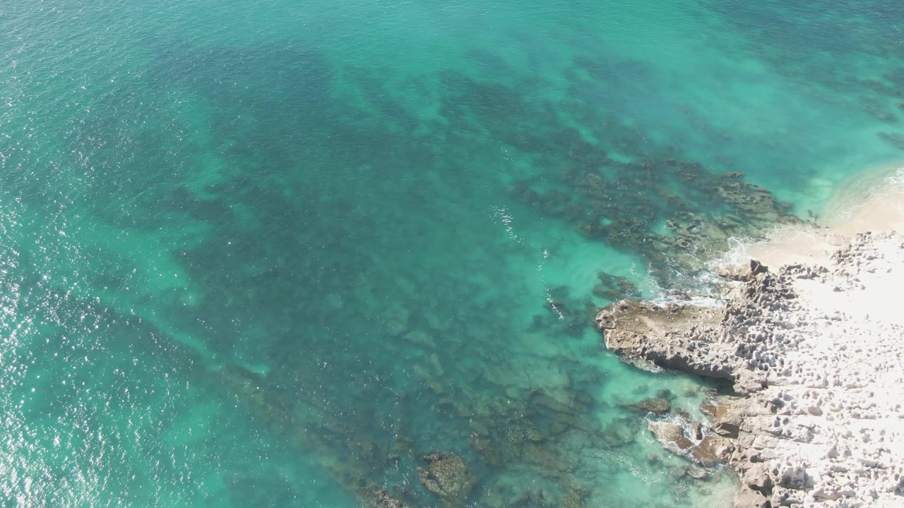 Clear shallow ocean with submerged rocks and pale rocky shore.