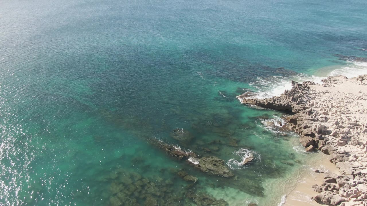 Aerial view of turquoise ocean meeting a rocky sandy shoreline.