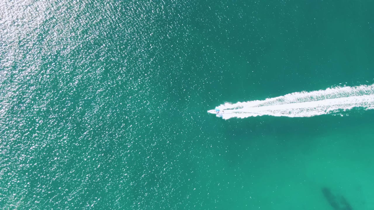At Buzzards Beach in Baja California Sur, a small speedboat runs across turquoise water near the upper right, leaving a white wake behind it, with no visible people.