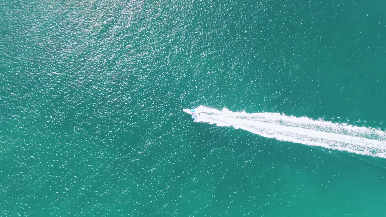 Speedboat wake crossing turquoise water from an overhead view.