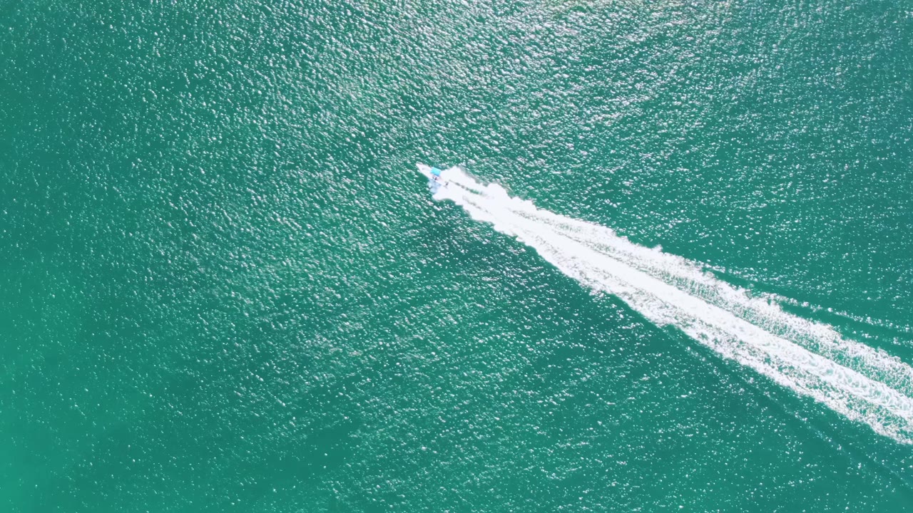 At Buzzards Beach in Baja California Sur, the speedboat continues across the upper portion of the frame while its foamy wake widens behind it over textured turquoise water, with no visible people.