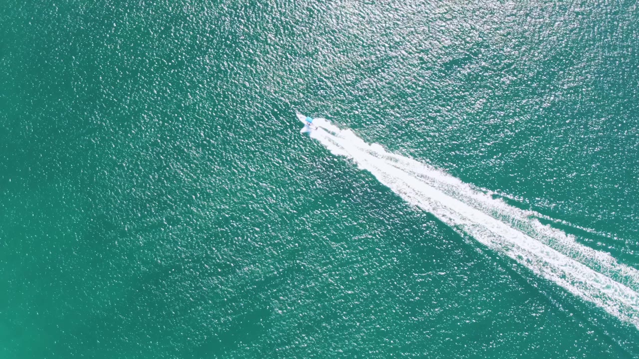 At Buzzards Beach in Baja California Sur, the speedboat sits farther toward the upper right edge and leaves a long white wake across the turquoise sea, with no visible people.