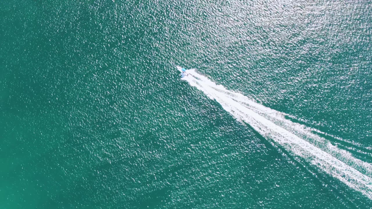 At Buzzards Beach in Baja California Sur, the speedboat cuts diagonally through green-blue water and pulls multiple bright wake lines behind it, with no visible people.