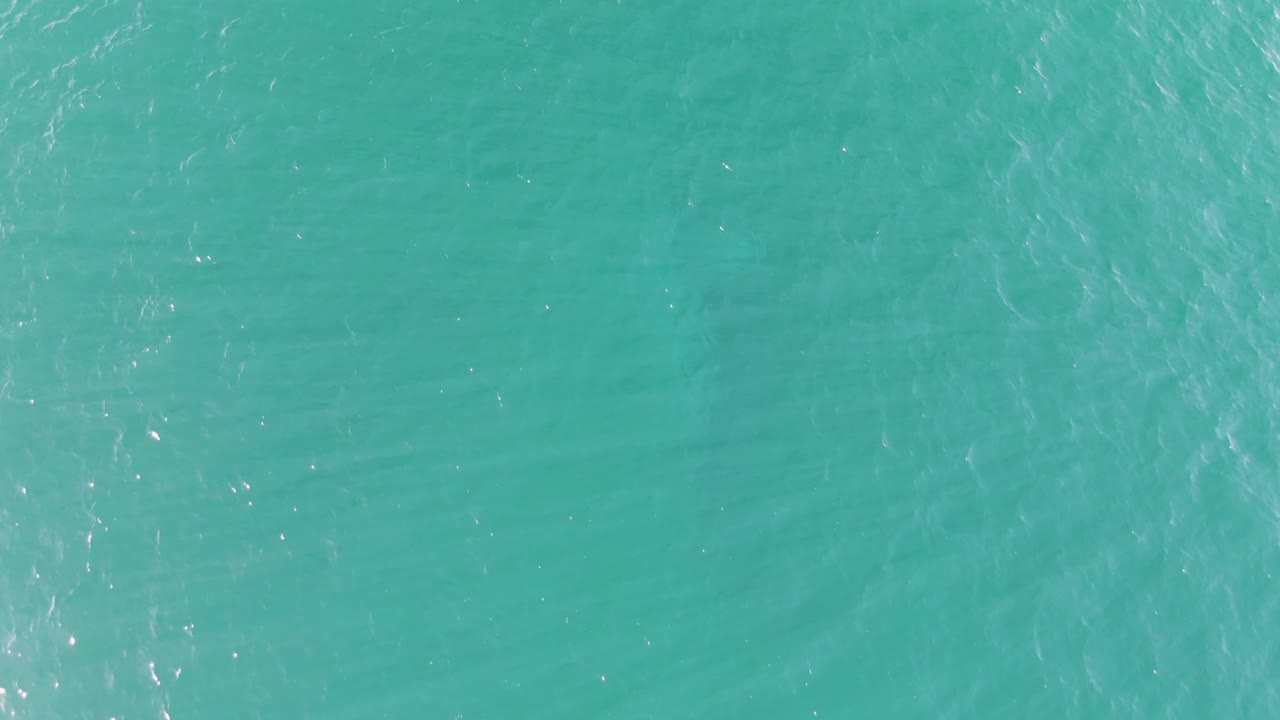 Clear blue-green ocean water at Buzzards Beach in Baja California Sur shows shifted ripple lines and scattered sunlight sparkles, with no visible people.