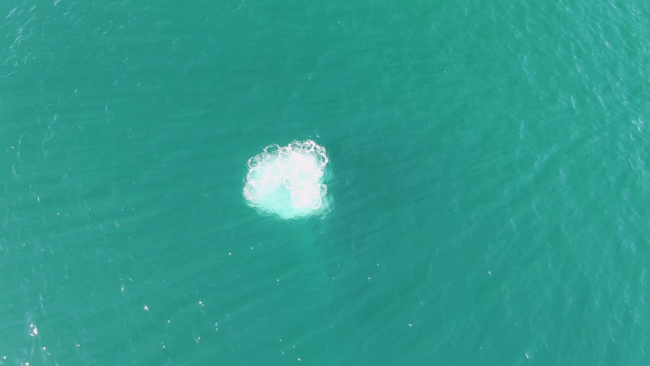 Overhead view at Buzzards Beach, Baja California Sur, showing a bright white splash in clear turquoise ocean water with no visible people.