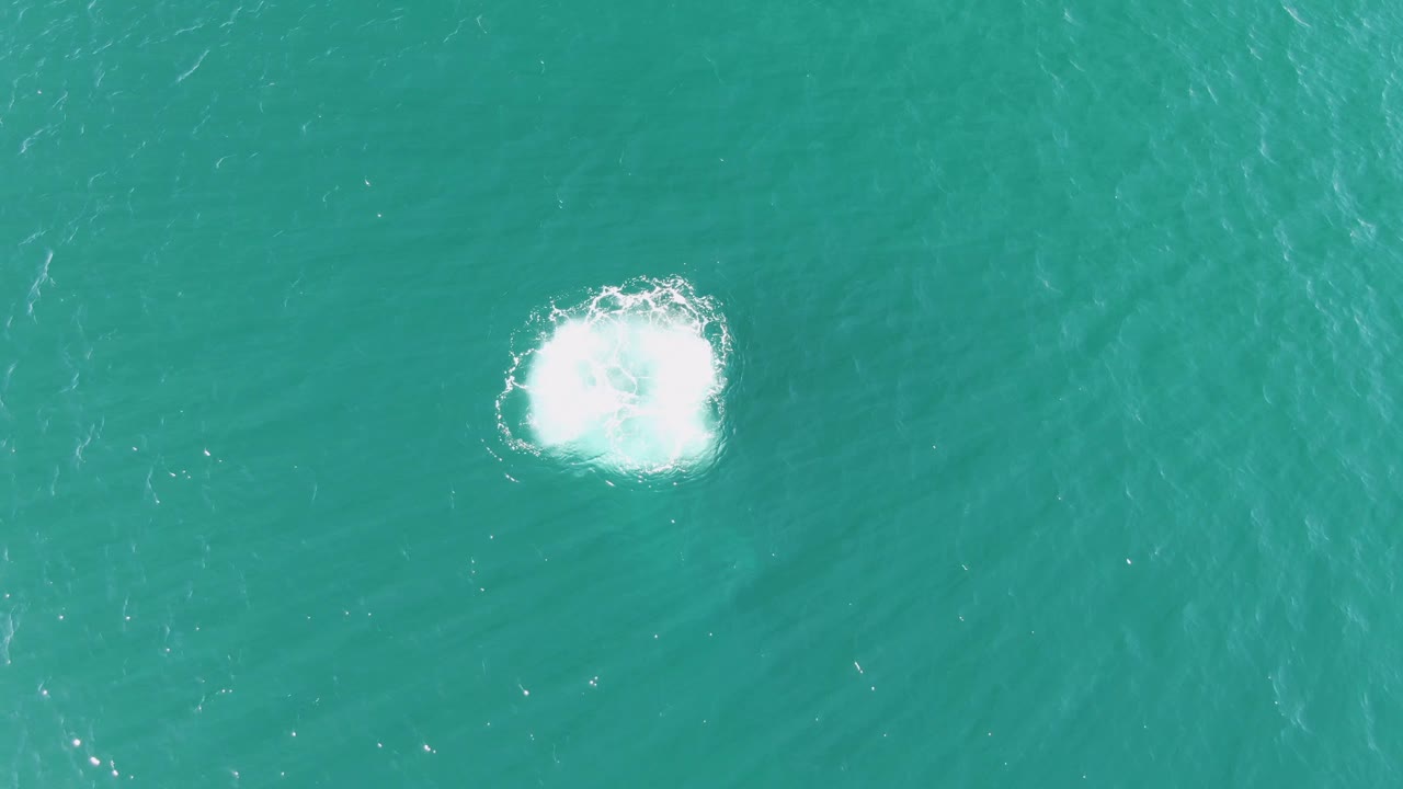 Later overhead frame at Buzzards Beach, Baja California Sur, showing the white foam patch persisting on clear turquoise water with no visible people.