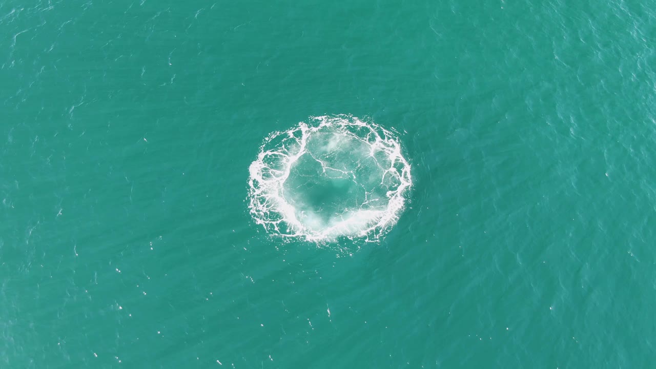 The circular splash has widened into a looser foam ring over turquoise sea at Buzzards Beach, Baja California Sur, with no visible people or objects.