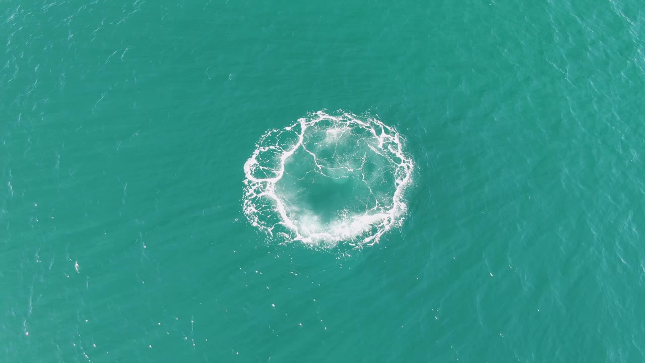 Late frame of the circular splash breaking into uneven white foam and ripples on turquoise ocean water at Buzzards Beach, with no visible people.