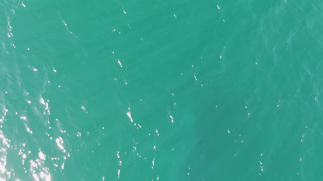 Overhead water view at Buzzards Beach with turquoise ripples, brighter sparkle clusters near the center and lower right, and no visible people.