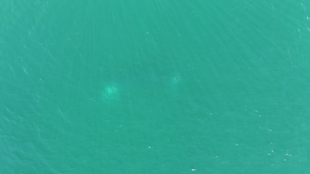 Turquoise ocean surface with two faint pale underwater light shapes.