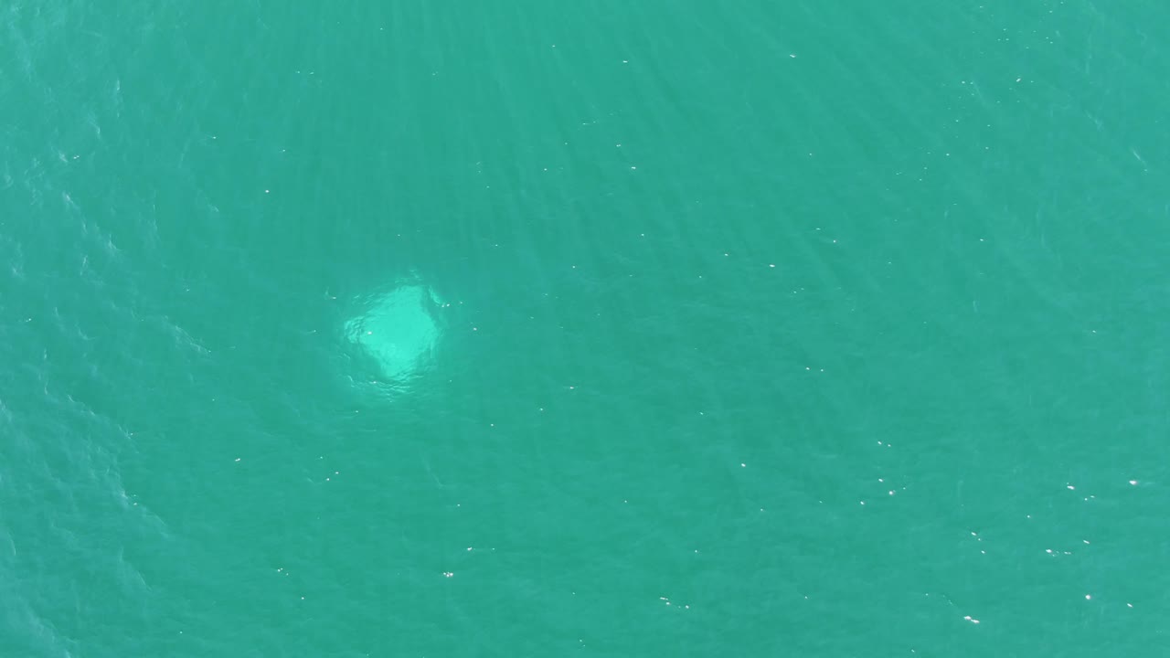 Top-down view of Buzzards Beach turquoise water with a brighter pale light patch toward the right side, soft ripples, and no visible people or boats.