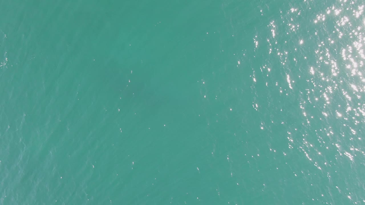 Bright turquoise ocean at Buzzards Beach with a denser vertical cluster of sun glints in the upper right and no visible people.