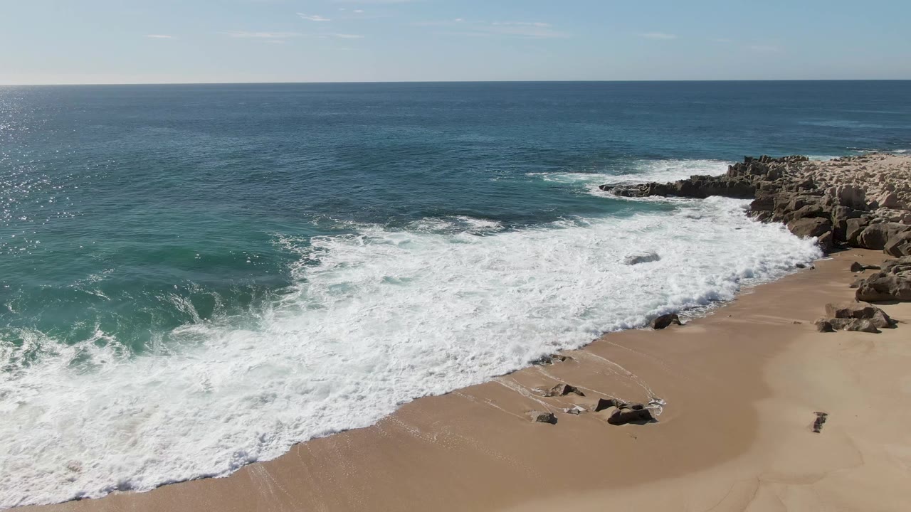 Aerial view of waves breaking onto sandy beach beside rocky outcrops