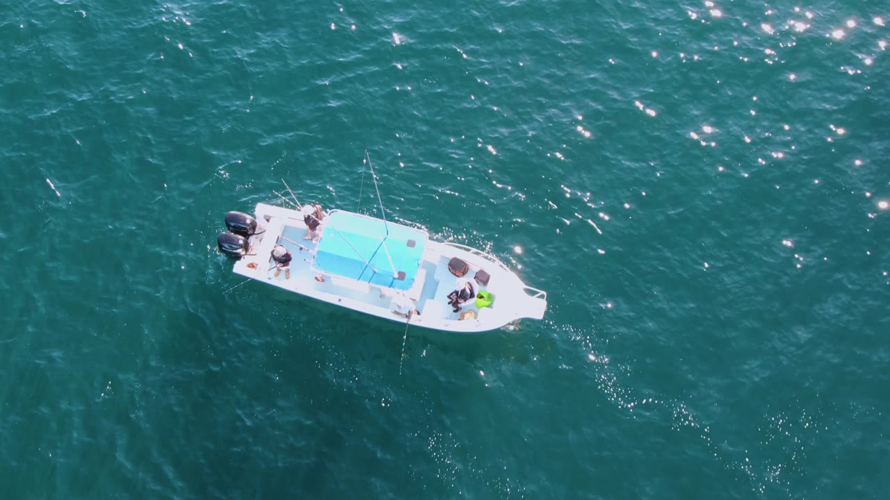 White canopy boat drifting across teal water with passengers aboard.