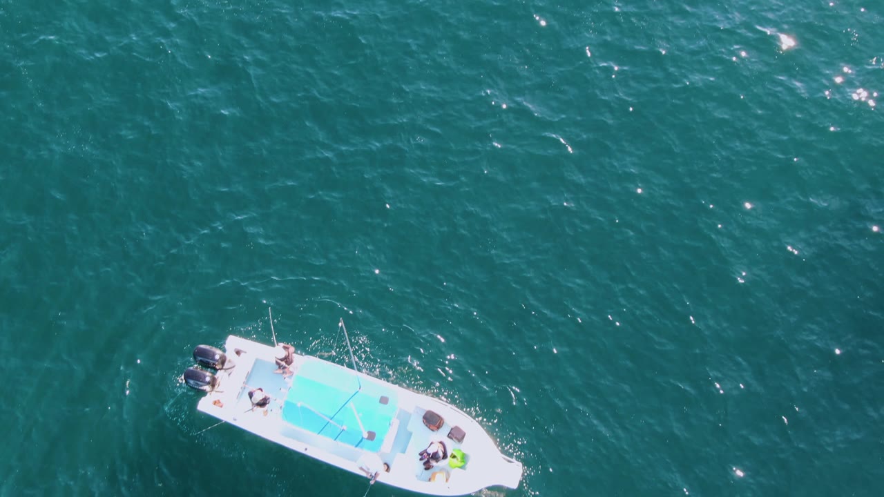 Overhead view of a white motorboat near Buzzards Beach, Baja California Sur, with a blue deck area, small people aboard, and sun flecks across turquoise water.