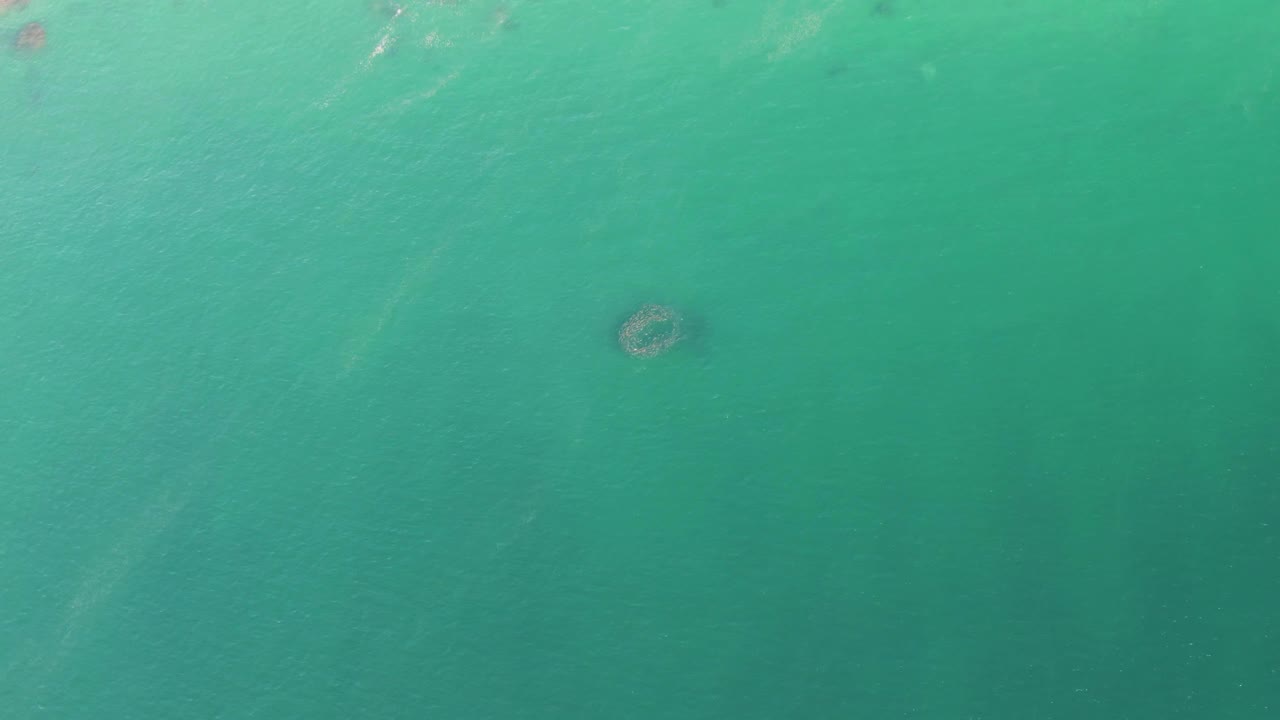 Fourth frame of the Baja California Sur water shot, with the dark round patch lower in the composition and faint pale streaks through the turquoise surface, no visible people.