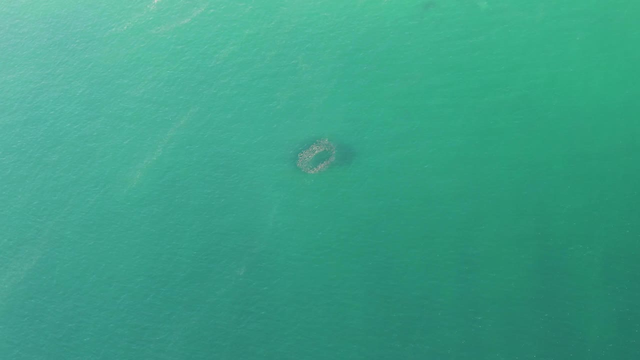 Overhead view of turquoise water at Buzzards Beach, Baja California Sur, with a small submerged dark structure near the upper center-left and no visible people.