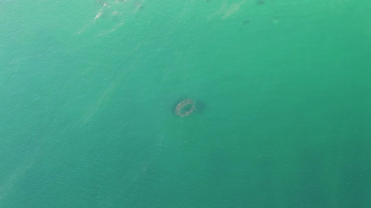 Overhead view of turquoise water at Buzzards Beach, Baja California Sur, with a small circular submerged structure left of center and no visible people.