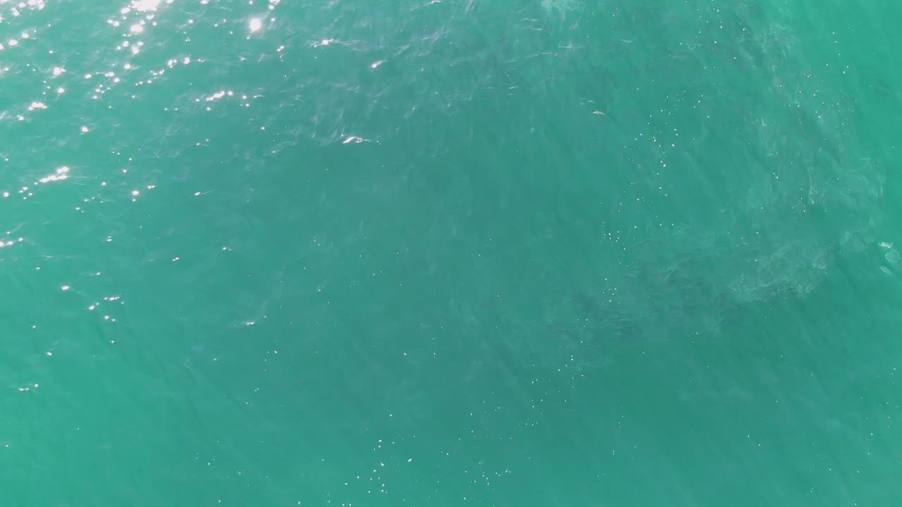Turquoise ocean water at Buzzards Beach, Baja California Sur, with left-side sunlight sparkle, soft wave lines across the frame, and no visible people.