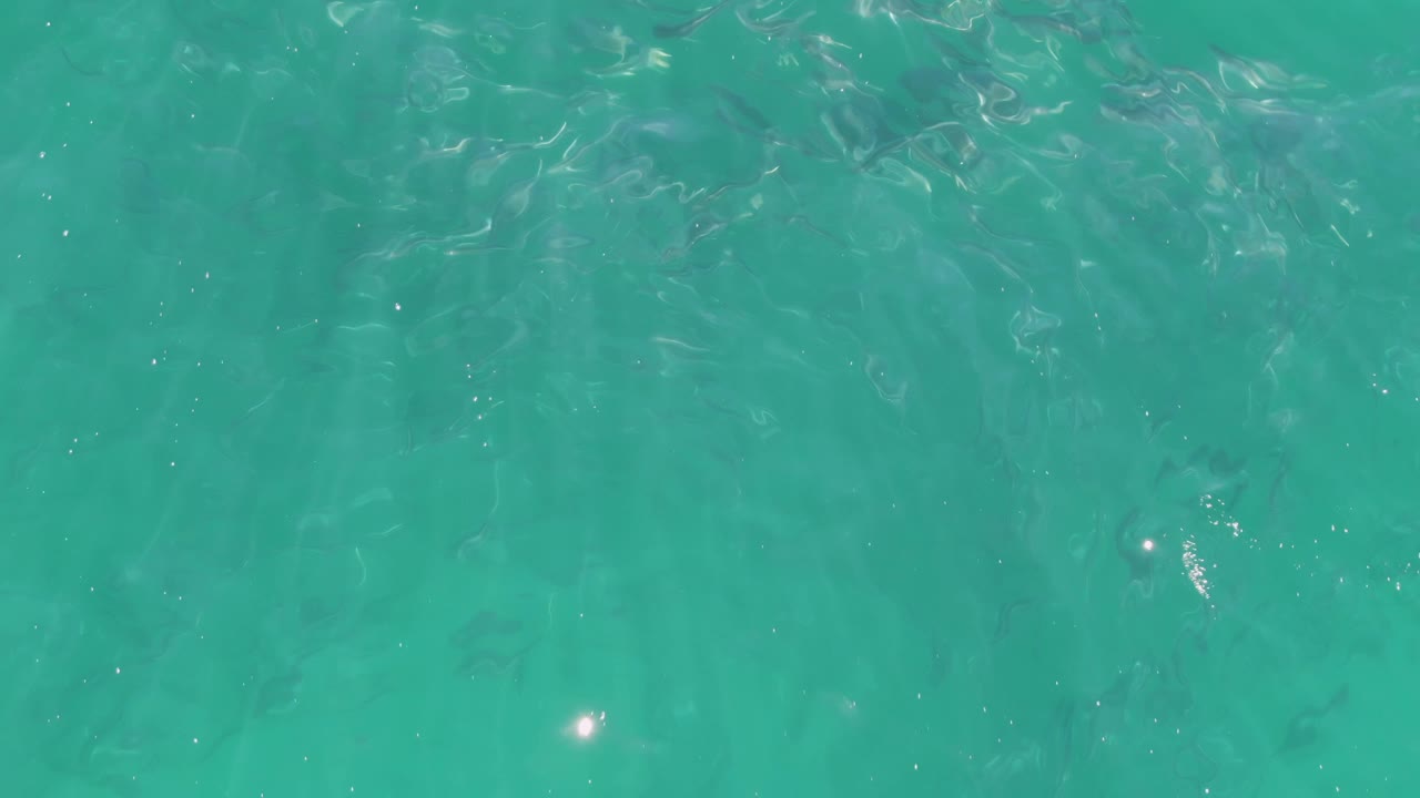 Overhead turquoise ocean water with ripples and sun reflections.