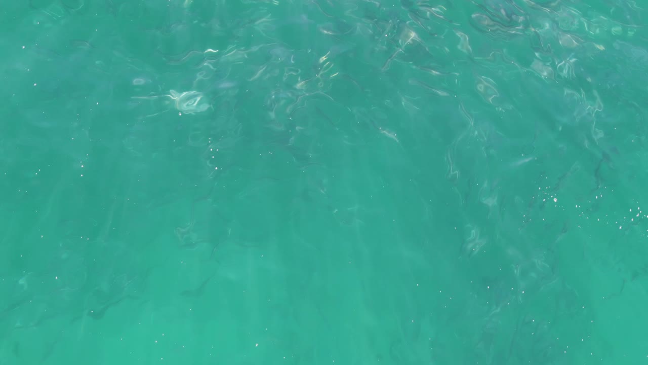 Clear shallow turquoise water at Buzzards Beach in Baja California Sur shows soft wave patterns, subtle sand color below, and no visible people.