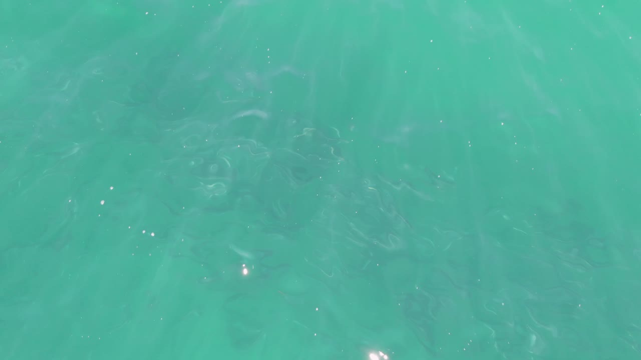 Clear aqua water at Buzzards Beach in Baja California Sur, with a few bright glints near the lower portion and no visible people.