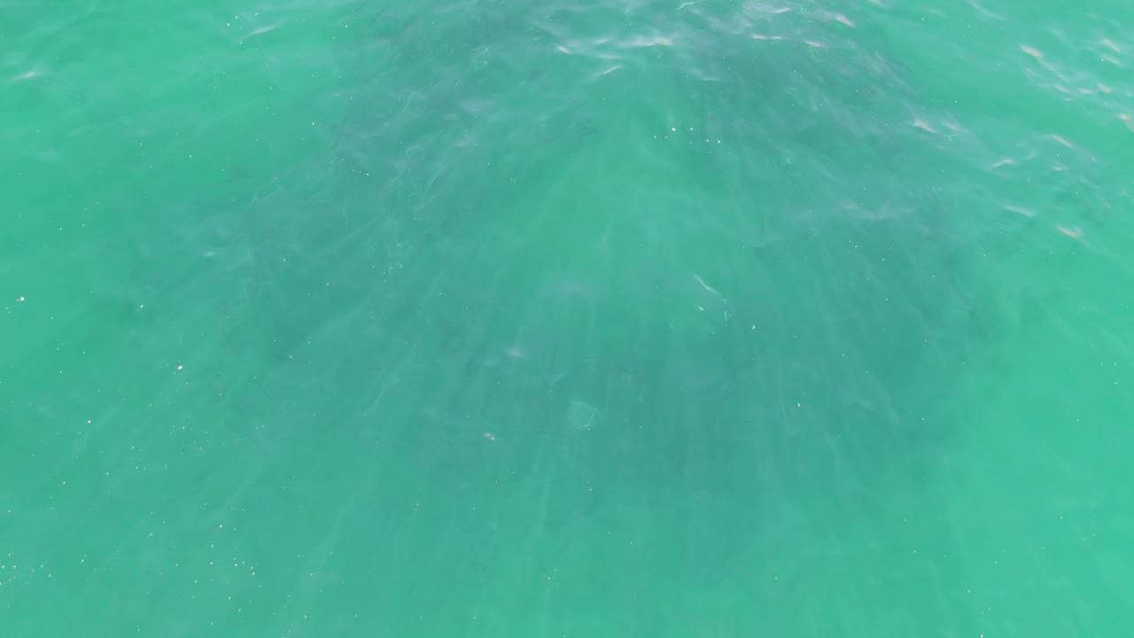Turquoise ocean at Buzzards Beach shows a more even field of ripple lines and muted sunlight shimmer, with no visible people or objects.