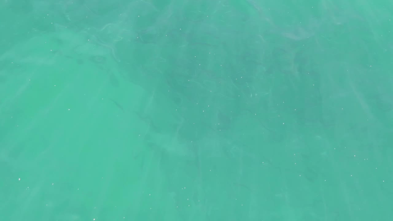Overhead view of clear turquoise water at Buzzards Beach, Baja California Sur, with faint sand patterns below and no visible people.