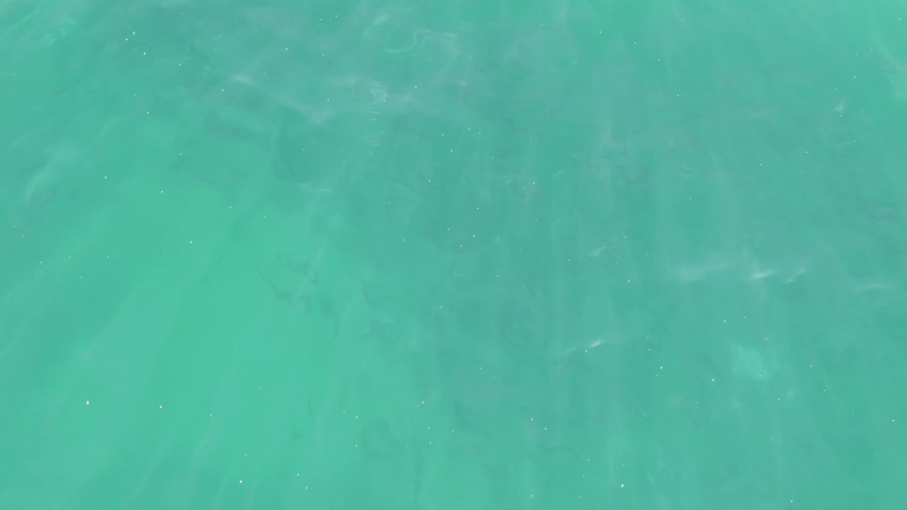 Clear blue-green ocean water at Buzzards Beach with subtle ripple bands crossing a sandy seabed and no visible people.