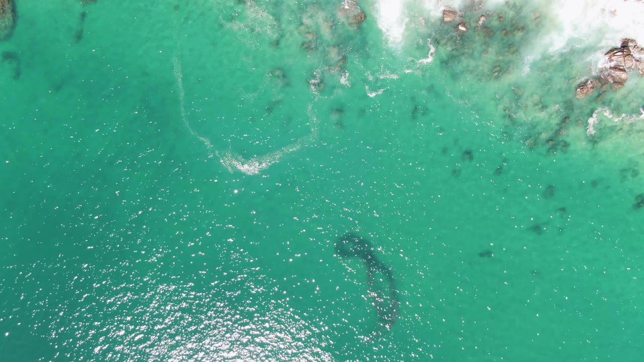 Turquoise ocean surface with surf foam and rocks along the upper edge.