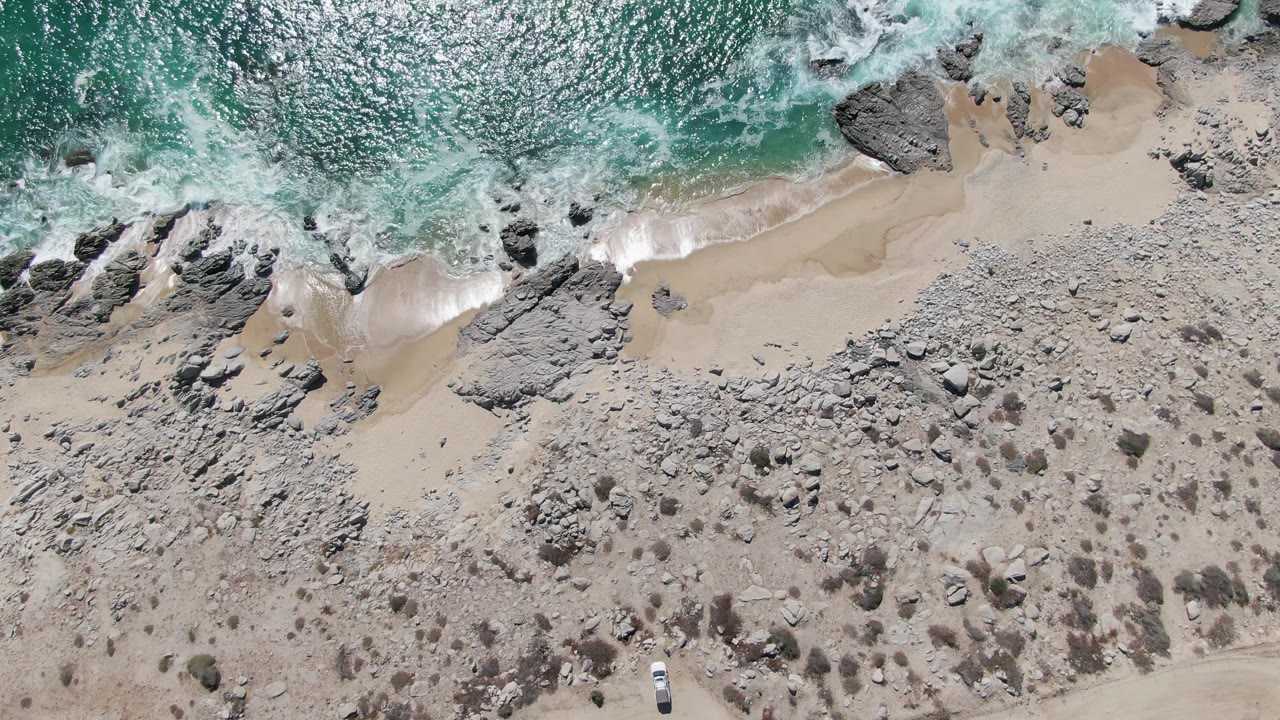 Overhead view of turquoise surf breaking onto a rocky sandy beach.