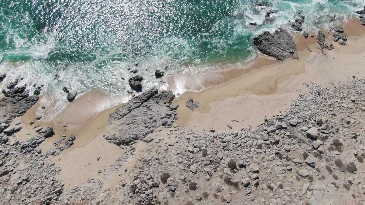 Turquoise wave wash over sand beside jagged shore rocks