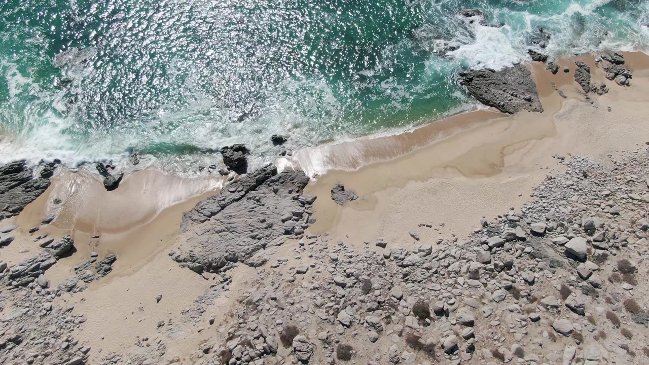 Overhead surf breaking across rocks and sand