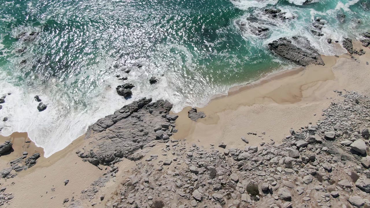 Overhead surf breaking across rocks and sand