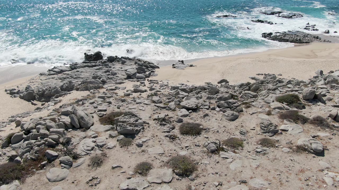 Wave wash reaches the sandy shoreline beside clusters of coastal boulders.
