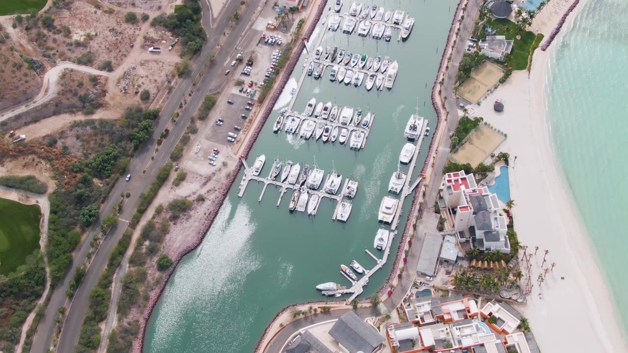 Cars on a coastal road beside a marina filled with docked boats.