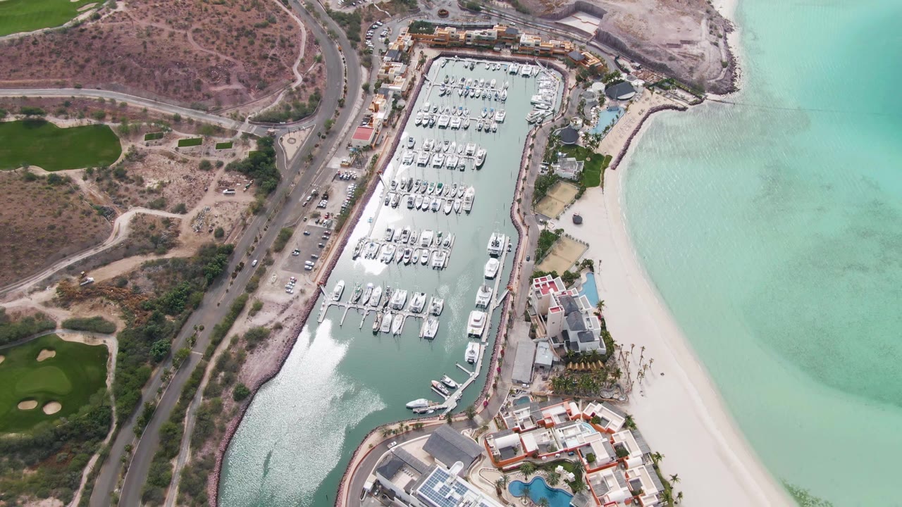 Aerial view of marina, beach, water, road, and hillside paths.