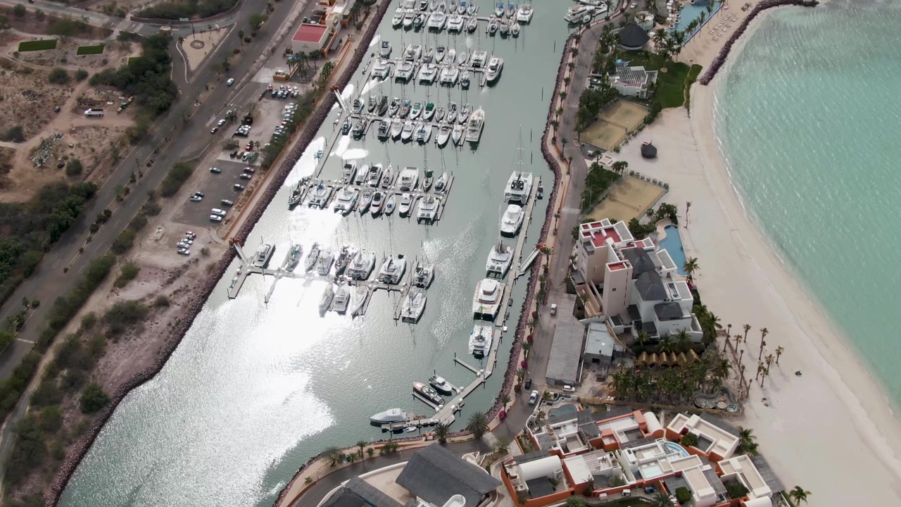 Overhead marina with rows of boats, road, beach, and coastal buildings.