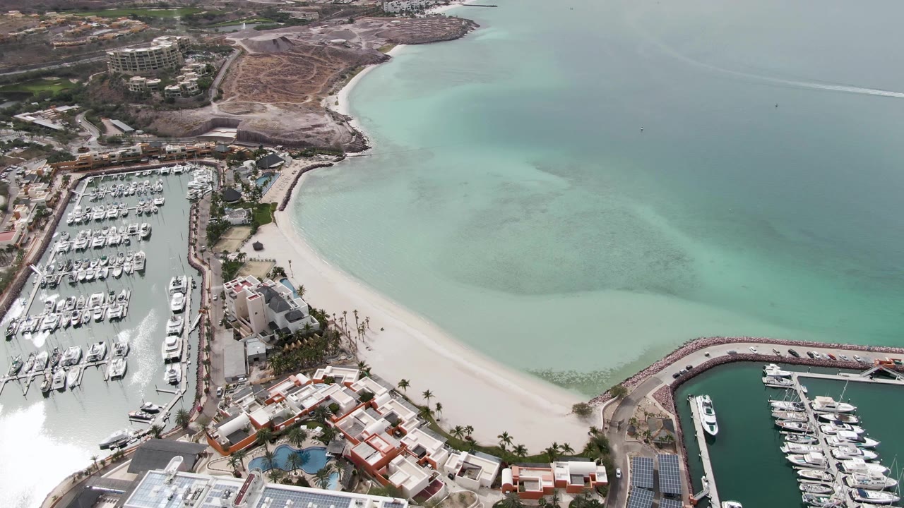 High aerial of marina, beach, coastal buildings, and turquoise bay water