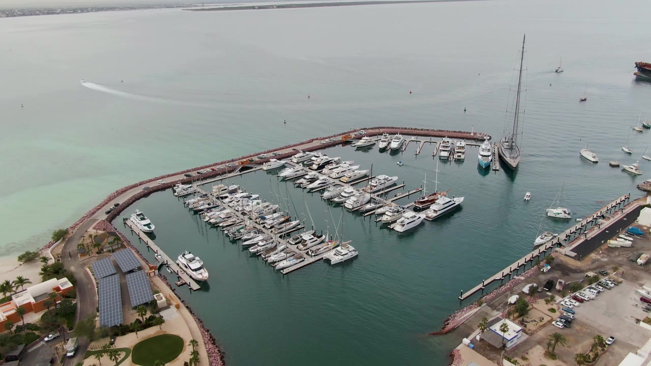 One second into the clip, the La Paz marina remains centered with docked yachts, a shoreline parking area, solar-panel roofs, a pier to the right, and no visible people.