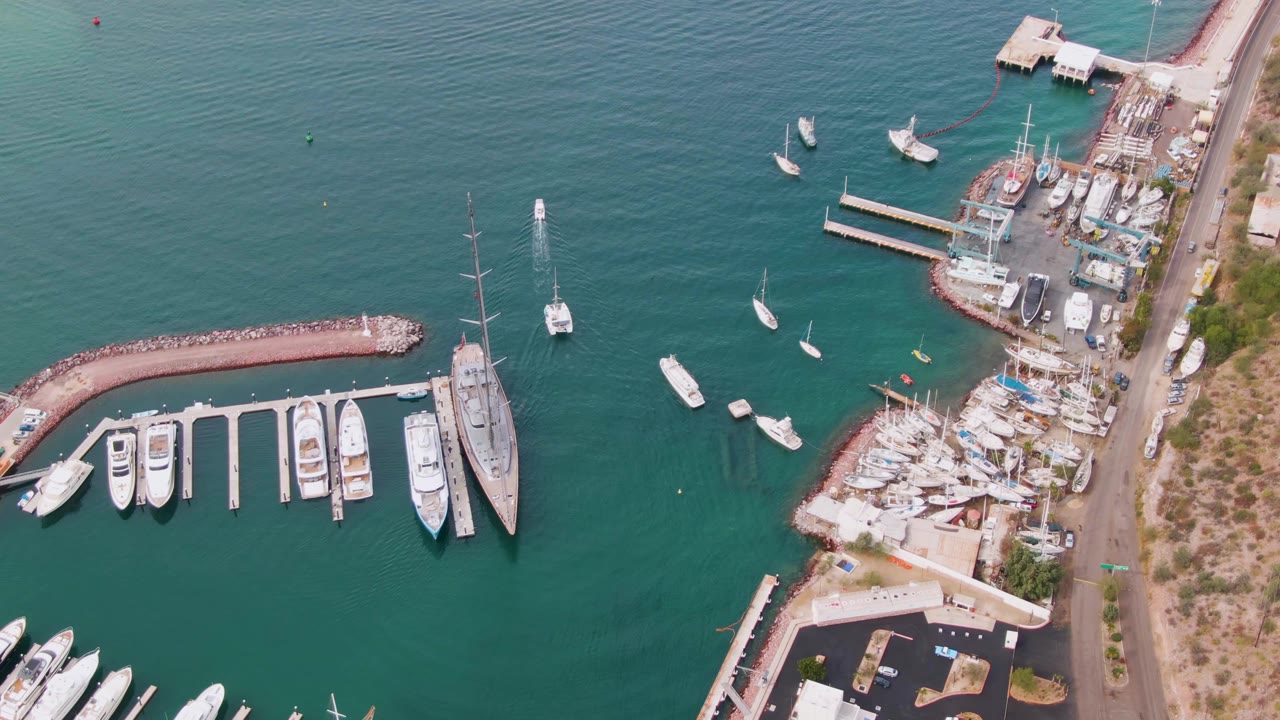 One second into the La Paz marina clip, the overhead view holds docked vessels by the slips while several small boats sit in open harbor water, with no visible people.