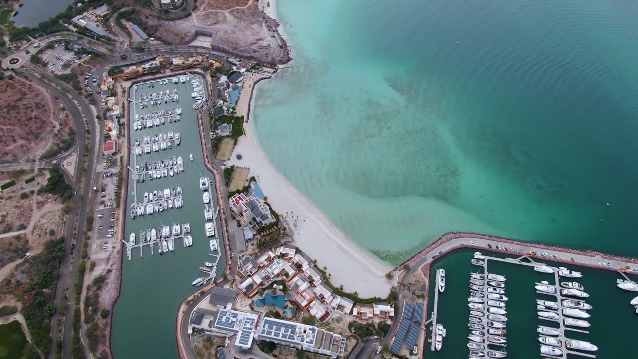 Aerial view of marina docks beside a pale beach and shallow water.