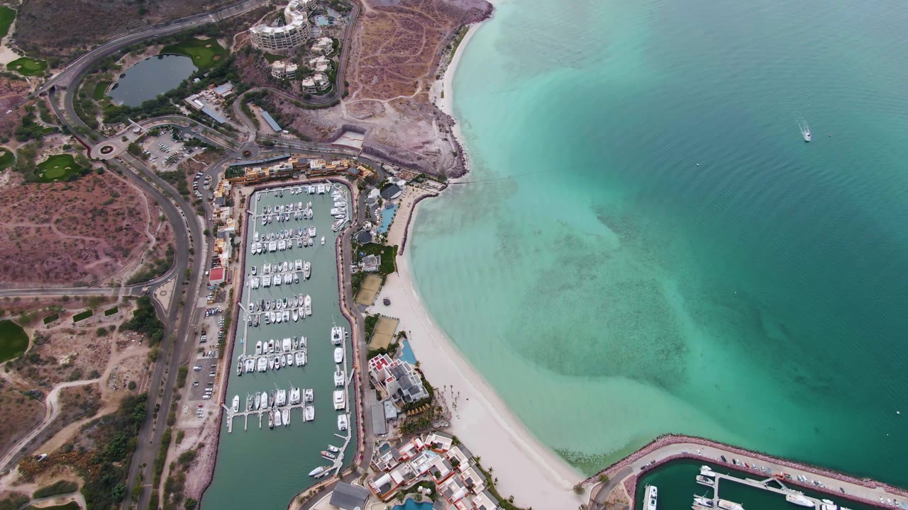 Drone view of marina slips, sandy shore, and broad turquoise bay.