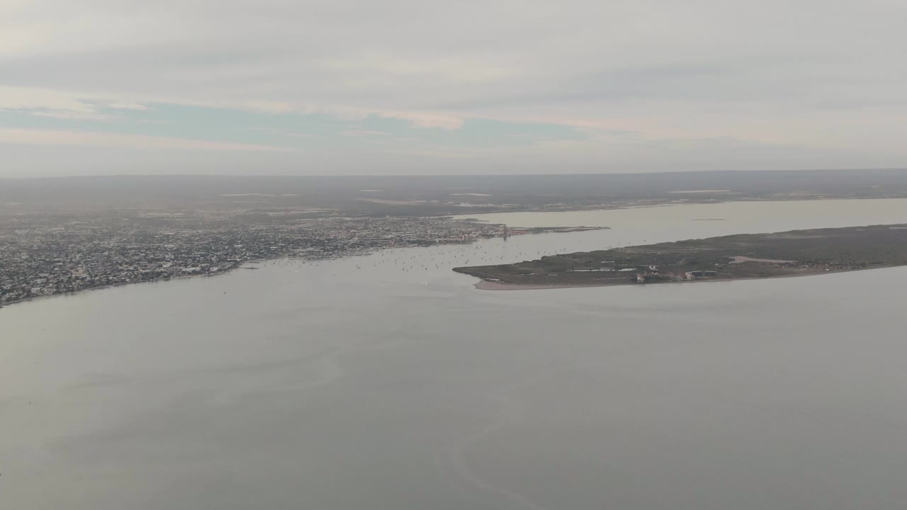 Wide aerial view of bay water, island, city shoreline, and overcast sky.