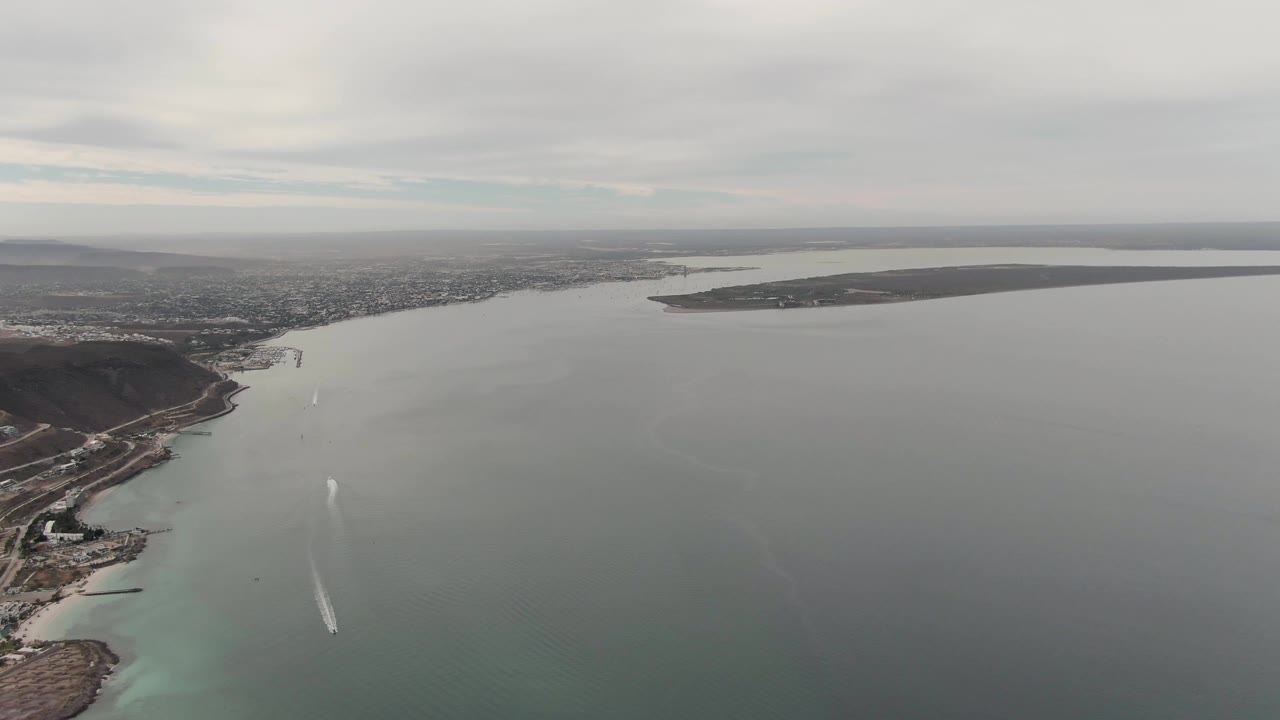 Aerial view of broad water, dark coastal hills, and a white boat wake.