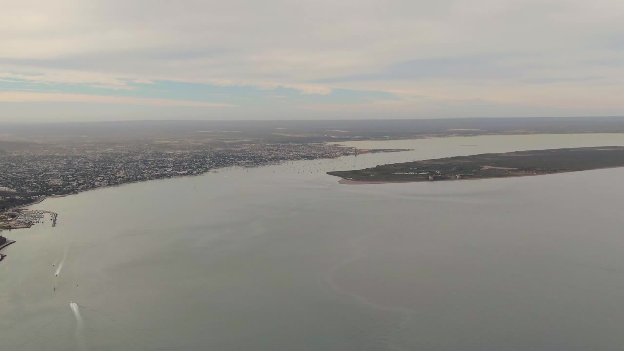 Aerial view across bay water toward dense shoreline development and distant land.
