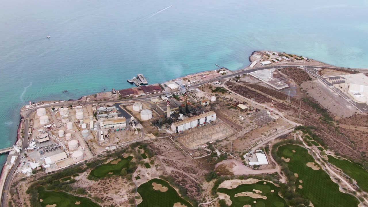 Aerial view of industrial shoreline, turquoise water, and green fields.